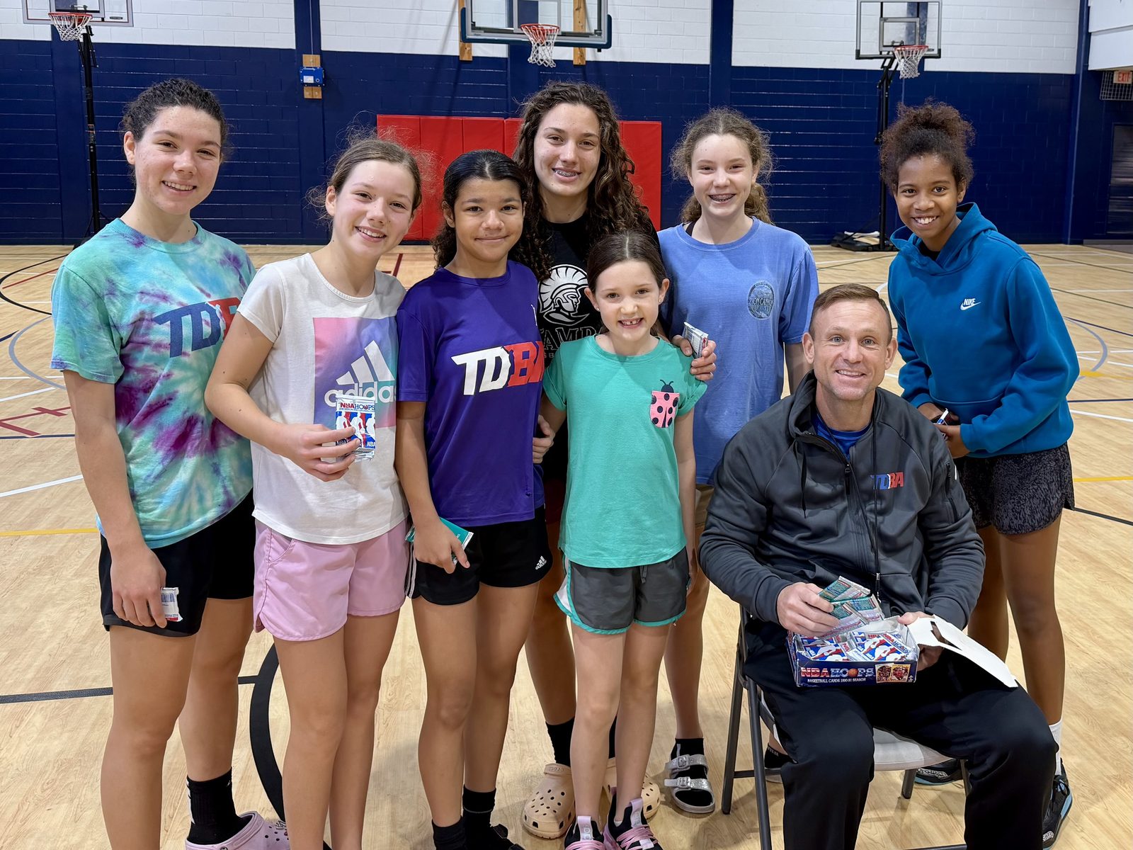 Girls at TDBA with Coach Teddy holding basketball card prizes after class