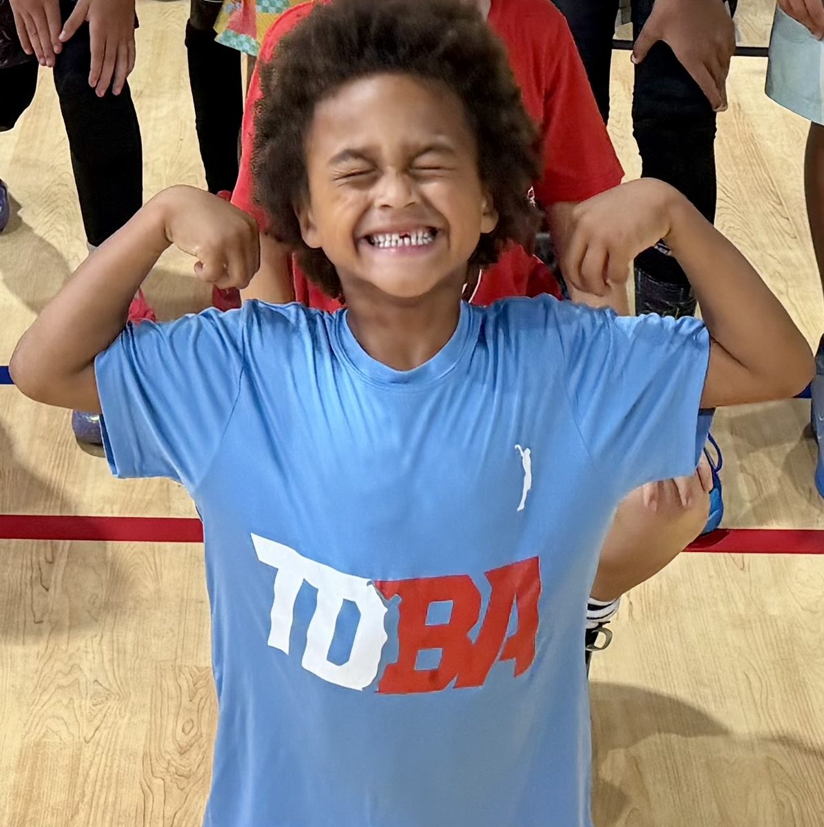A young TDBA player in a TDBA shirt flexing and grinning after a drill